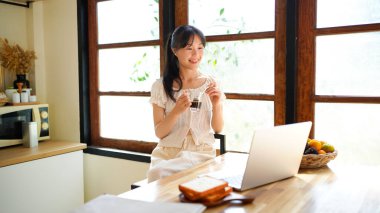 Genç iş kadını uzaktan iş yönetiyor, dizüstü bilgisayar kullanıyor sabahları mutfak tezgahında oturuyor, kişisel gelişim üzerine çalışıyor..
