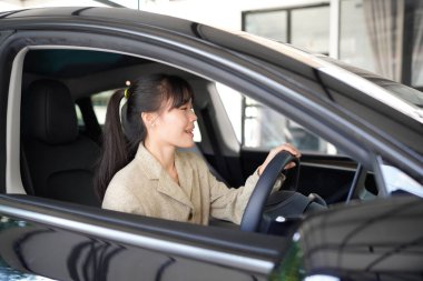 Kahverengi takım elbiseli genç ve çekici bir iş kadını lüks arabasıyla araba sürüyor ve gülümsüyor. İş ulaşımı kavramı.