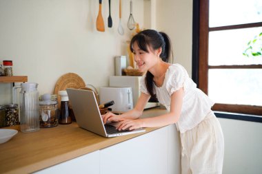 Genç iş kadını uzaktan kumandalı, serbest çalışan bir kadın sabahları mutfak tezgahında dizüstü bilgisayar kullanıyor ve kişisel gelişim üzerine çalışıyor..