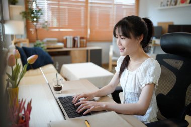 Masada otururken rahat ev oturma odasında dizüstü bilgisayarda çalışan bir kadın. Serbest çalışan kadın sosyal ağlarda internette sohbet ediyor..