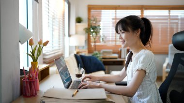 Masada otururken rahat ev oturma odasında dizüstü bilgisayarda çalışan bir kadın. Serbest çalışan kadın sosyal ağlarda internette sohbet ediyor..