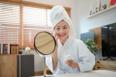 Kadınlar evde bornoz ve havlu giyer cilt bakımını gençleştirir, aynaya bakar. Günlük güzellik rutini.