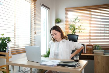 Sırtı ağrıyan bir bayan girişimci evde çalışırken sırtına masaj yapıyor..