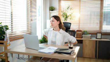 Sırtı ağrıyan bir bayan girişimci evde çalışırken sırtına masaj yapıyor..