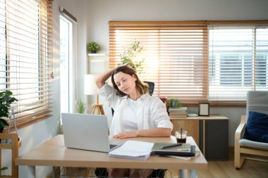 Beyaz kadın evden çalışırken kollarını uzatıyor, dizüstü bilgisayarla uzun süre çalıştıktan sonra mola veriyor..