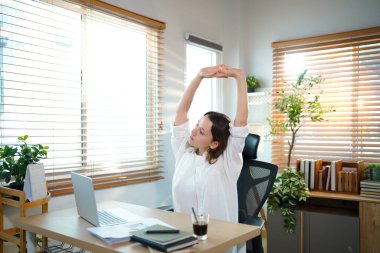 Beyaz kadın evden çalışırken kollarını uzatıyor, dizüstü bilgisayarla uzun süre çalıştıktan sonra mola veriyor..