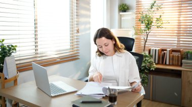 Merkez ofisteki kadın, uzaktan çalışma, fikirler ve düşünme üzerine araştırma yapmak için belgeler ve dizüstü bilgisayar. Bilgisayarlı mutlu kız, notlar yazıyor ve evde serbest ağ arayışı yapıyor..