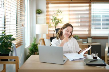 Merkez ofisteki kadın, uzaktan çalışma, fikirler ve düşünme üzerine araştırma yapmak için belgeler ve dizüstü bilgisayar. Bilgisayarlı mutlu kız, notlar yazıyor ve evde serbest ağ arayışı yapıyor..