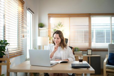 Merkez ofisteki kadın, uzaktan çalışma, fikirler ve düşünme üzerine araştırma yapmak için belgeler ve dizüstü bilgisayar. Bilgisayarlı mutlu kız, notlar yazıyor ve evde serbest ağ arayışı yapıyor..