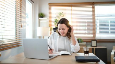 Merkez ofisteki kadın, uzaktan çalışma, fikirler ve düşünme üzerine araştırma yapmak için belgeler ve dizüstü bilgisayar. Bilgisayarlı mutlu kız, notlar yazıyor ve evde serbest ağ arayışı yapıyor..