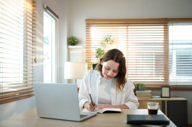 Merkez ofisteki kadın, uzaktan çalışma, fikirler ve düşünme üzerine araştırma yapmak için belgeler ve dizüstü bilgisayar. Bilgisayarlı mutlu kız, notlar yazıyor ve evde serbest ağ arayışı yapıyor..
