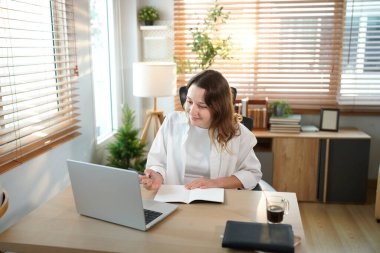 Merkez ofisteki kadın, uzaktan çalışma, fikirler ve düşünme üzerine araştırma yapmak için belgeler ve dizüstü bilgisayar. Bilgisayarlı mutlu kız, notlar yazıyor ve evde serbest ağ arayışı yapıyor..