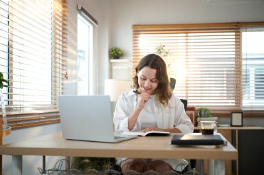 Merkez ofisteki kadın, uzaktan çalışma, fikirler ve düşünme üzerine araştırma yapmak için belgeler ve dizüstü bilgisayar. Bilgisayarlı mutlu kız, notlar yazıyor ve evde serbest ağ arayışı yapıyor..