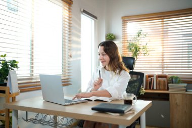 Merkez ofisteki kadın, uzaktan çalışma, fikirler ve düşünme üzerine araştırma yapmak için belgeler ve dizüstü bilgisayar. Bilgisayarlı mutlu kız, notlar yazıyor ve evde serbest ağ arayışı yapıyor..