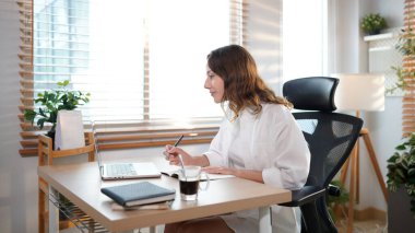 Merkez ofisteki kadın, uzaktan çalışma, fikirler ve düşünme üzerine araştırma yapmak için belgeler ve dizüstü bilgisayar. Bilgisayarlı mutlu kız, notlar yazıyor ve evde serbest ağ arayışı yapıyor..