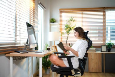 Kadın merkez ofis çalışanlarının çalışma alanı. Kadın açık güneşli odada bilgisayarla kitap okuyor. Modern tasarım.