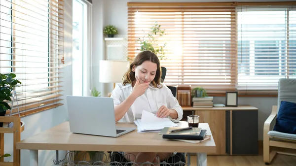 Merkez ofisteki kadın, uzaktan çalışma, fikirler ve düşünme üzerine araştırma yapmak için belgeler ve dizüstü bilgisayar. Bilgisayarlı mutlu kız, notlar yazıyor ve evde serbest ağ arayışı yapıyor..