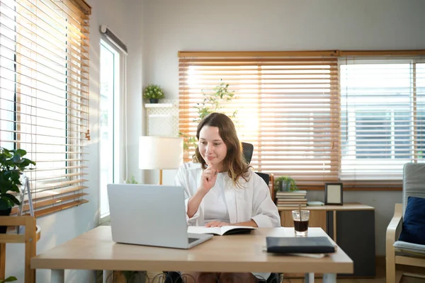 Merkez ofisteki kadın, uzaktan çalışma, fikirler ve düşünme üzerine araştırma yapmak için belgeler ve dizüstü bilgisayar. Bilgisayarlı mutlu kız, notlar yazıyor ve evde serbest ağ arayışı yapıyor..