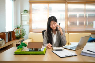 Asyalı emlakçı müvekkil telefon görüşmesi ev satışları profesyonel iş iletişimi modern ofis ayarları tartışması.