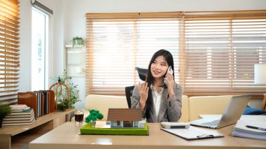 Asyalı emlakçı müvekkil telefon görüşmesi ev satışları profesyonel iş iletişimi modern ofis ayarları tartışması.