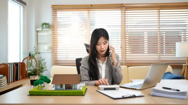 Asyalı emlakçı müvekkil telefon görüşmesi ev satışları profesyonel iş iletişimi modern ofis ayarları tartışması.