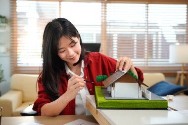 Ofisinde kâğıt çizen bir mimari model üzerinde çalışan genç bir mimar modern ofiste model ev inşa eden genç bir kadın..