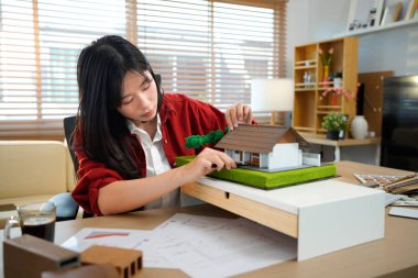 Ofisinde kâğıt çizen bir mimari model üzerinde çalışan genç bir mimar modern ofiste model ev inşa eden genç bir kadın..