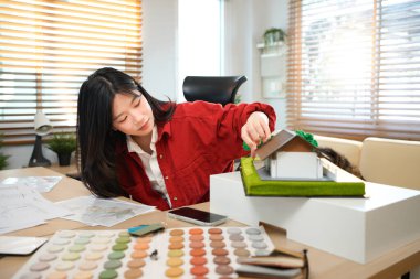 Ofisinde kâğıt çizen bir mimari model üzerinde çalışan genç bir mimar modern ofiste model ev inşa eden genç bir kadın..