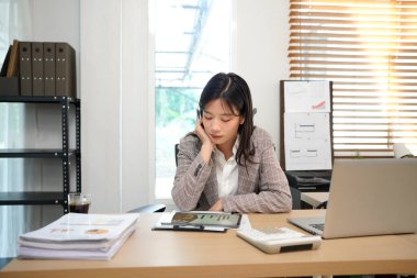 Profesyonel iş kadını kıyafeti, masasındaki dijital tabletteki verileri, modern hibrit ofis çalışma alanında odaklanmış ve üretken bir bilgisayarla gözden geçiriyor..