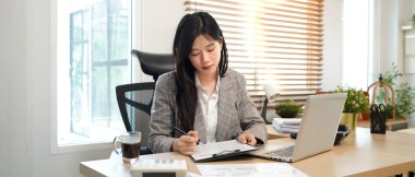 Güzel Asyalı genç iş kadını dizüstü bilgisayar ve kağıt işlerini kullanarak mali belge, vergi, döviz, muhasebe ve mali danışman üzerinde çalışıyor..