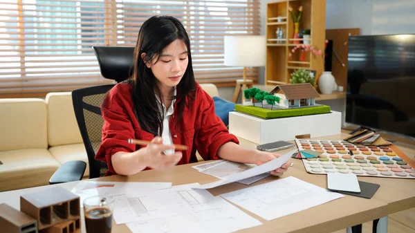 Genç Asyalı kadın mimar planlar üzerinde çalışıyor. Mühendis mimari planı inceliyor, bir inşaat projesi çiziyor. İş yerinde oturan bir kadının portresi. İş konsepti.