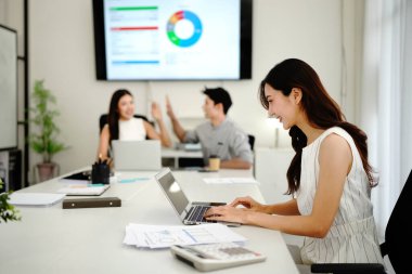 Toplantı odasında arka planda çalışan meslektaşlar bilgisayardan e-postaları okurken odaklanmış kadın yönetici.