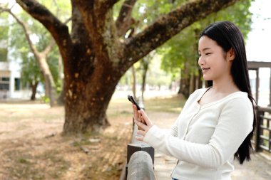 Happy Teenage girl browses smartphone online content in a park a sunny day.