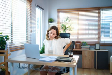 Sırtı ağrıyan bir bayan girişimci evde çalışırken sırtına masaj yapıyor..