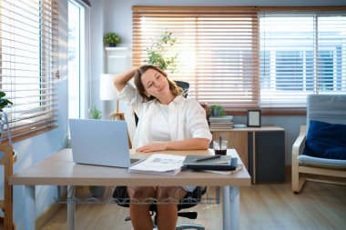 Beyaz kadın evden çalışırken kollarını uzatıyor, dizüstü bilgisayarla uzun süre çalıştıktan sonra mola veriyor..