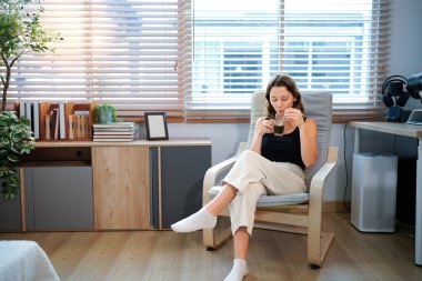 Kafkasyalı mutlu bir kadın tatil sabahı sıcak kahve ya da çay içerek evdeki koltukta dinleniyor, rahat bir sahne, sıcak çay içen güzel bir kadın..