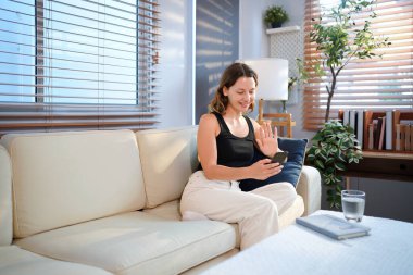 Evdeki kanepede oturan ve selfie çeken genç bir kadın..