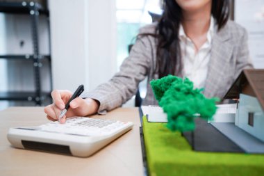 Ev modelli iş ipoteği emlakçısı, masada oturuyor, emlakçı hesap makinesi ve belgeler, ipotek ve mülk üzerinde çalışıyor..