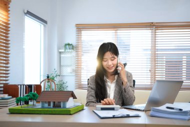 Asyalı emlakçı müvekkil telefon görüşmesi ev satışları profesyonel iş iletişimi modern ofis ayarları tartışması.