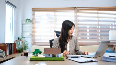 Gayrimenkul ile Ev Anlaşması, çekici, dengeli bir bayan ajan anlaşmanın ayrıntılarını araştırır, evrakları dikkatlice inceler. Yakınlarda bir model ev var, deneğin elle tutulur bir sembolü..