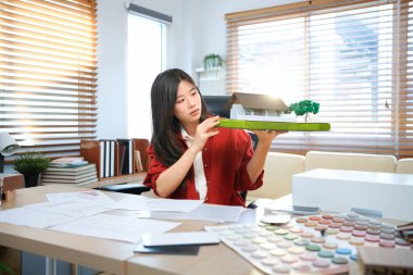 Ofisinde kâğıt çizen bir mimari model üzerinde çalışan genç bir mimar modern ofiste model ev inşa eden genç bir kadın..