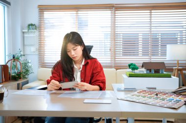 Genç Asyalı kadın mimar planlar üzerinde çalışıyor. Mühendis mimari planı inceliyor, bir inşaat projesi çiziyor. İş yerinde oturan bir kadının portresi. İş konsepti.
