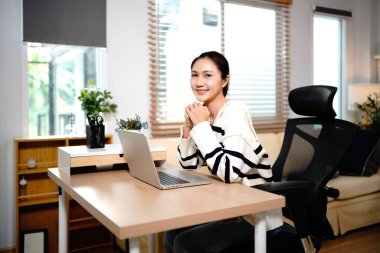 Güzel Asyalı bir kadının portresi ev bilgisayarında çalışırken gülümseyen yüzüyle kameraya bakarken bilgisayardaki noter kız başarı işi internet pazarlaması ile rahat bir şekilde oturuyor..