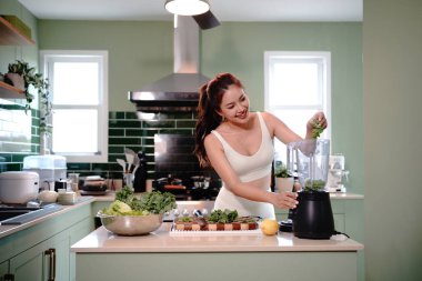 Genç Sportif kadın sağlıklı yeşil bir meyve püresi için taze lahana koyarken gülümsüyor. Yeşil detoks suyu konsepti.