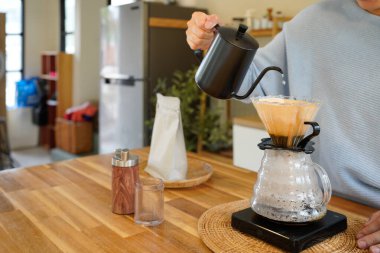 Genç Asyalı bir kadın, siyah çaydanlıktan kahve damlatıcısına sıcak su döküyor, modern mutfakta kadın kahvesi yapıyor, sabah yaşam tarzı, yavaş bar kafe ve ev yapımı konsept..