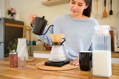 Genç Asyalı bir kadın, siyah çaydanlıktan kahve damlatıcısına sıcak su döküyor, modern mutfakta kadın kahvesi yapıyor, sabah yaşam tarzı, yavaş bar kafe ve ev yapımı konsept..
