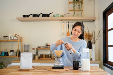 Genç bir kadın mutfakta el değirmeni ile kahve çekirdeklerini öğütüyor. Kahve çekirdeklerini toz haline getiren öğütücüyü döndürmek için döndürme kolu.