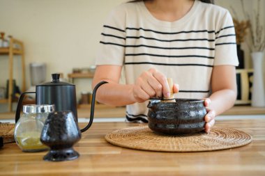 Geleneksel siyah bir kâse içinde, tahta bir masada, bir kadının kibrit çayını çırpışına yakın çekim. Sağlıklı yaşam tarzı ve sağlık kavramı.