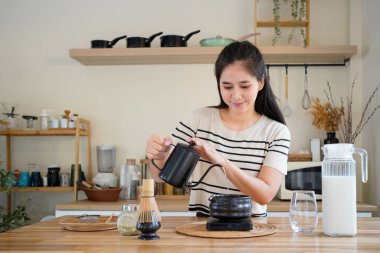 Genç bir kadın, sıcak bir mutfakta çay hazırlıyor geleneksel Japon çayı hazırlayan geleneksel bir kaseye sıcak su döküyor..