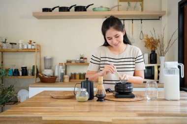 Genç Asyalı kadın geleneksel Japon kibrit tozu hazırlıyor ve mutfak evinde dijital ölçekte geleneksel siyah kibrit tozuna dönüştürüyor. Japon matcha..